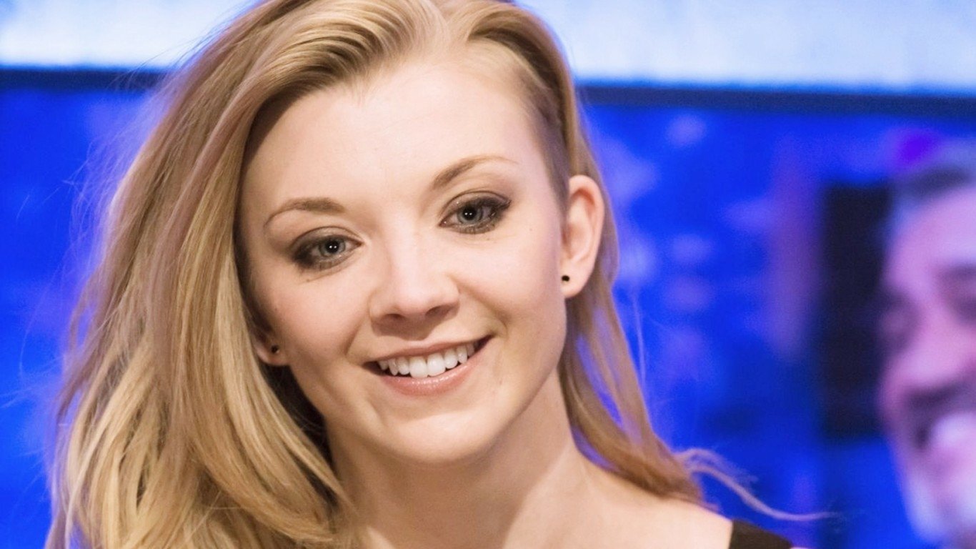 Portrait of celebrity Natalie Dormer smiling with a blurred blue and purple background.