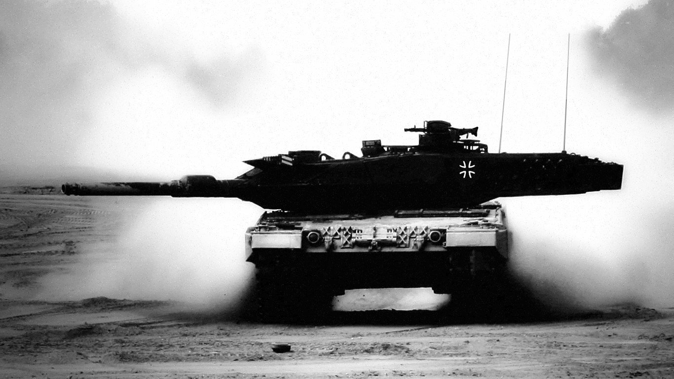 A Leopard 2 tank moves through a dusty terrain, showcasing its military prowess with a cloud of dust billowing around it, captured in striking black and white.