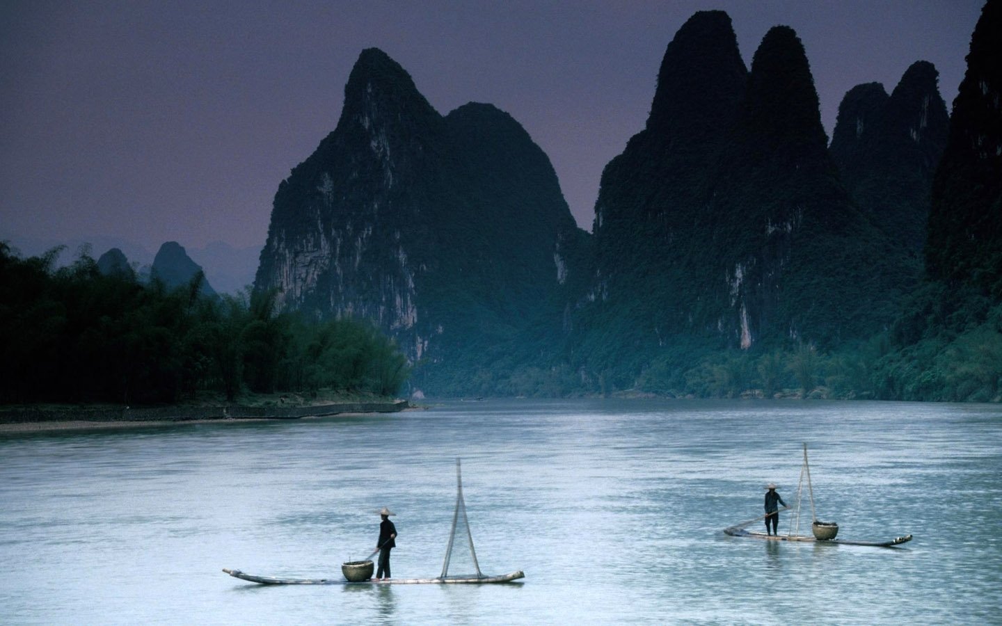 China landscape photography: two fishermen on bamboo rafts drifting on a misty river beneath towering karst peaks.