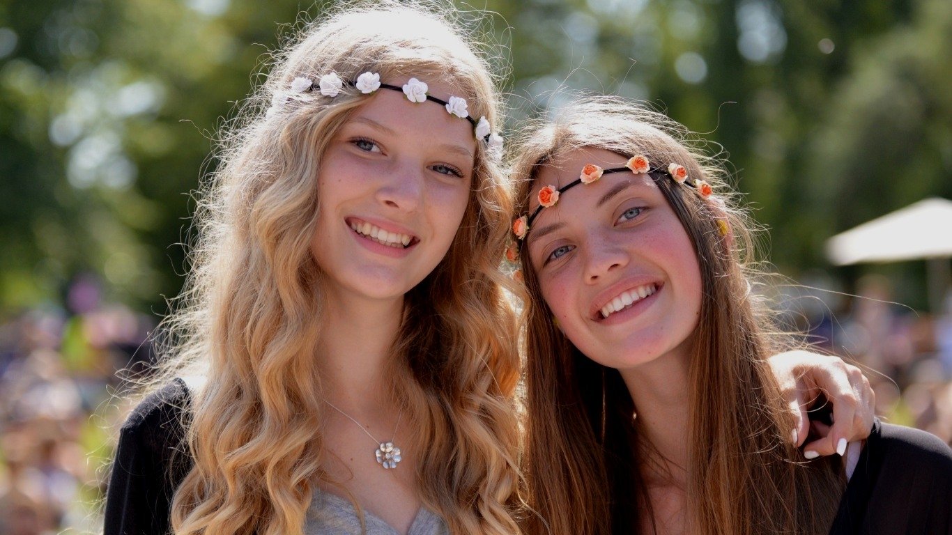 Two women with flower crowns smile warmly outdoors, radiating a joyful and relaxed mood.