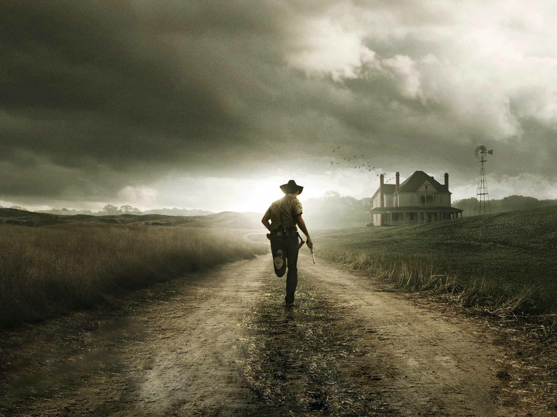 A lone figure resembling Rick Grimes from The Walking Dead walks down a desolate dirt road, with a farmhouse in the background under a dramatic sky.