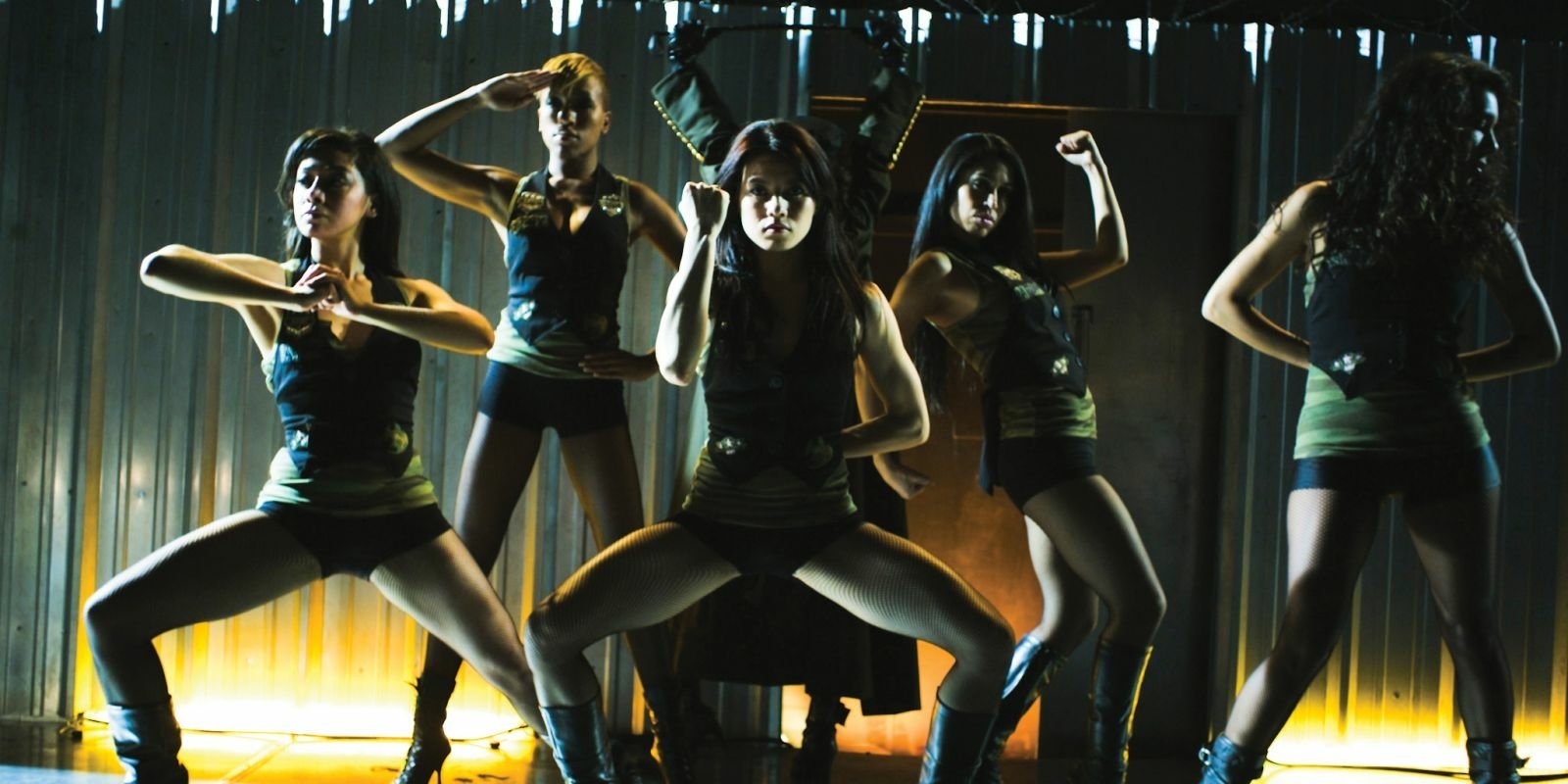 Five dancers in dark tank tops and shorts strike low, synchronized poses on a lit stage — scene from the movie Go For It.