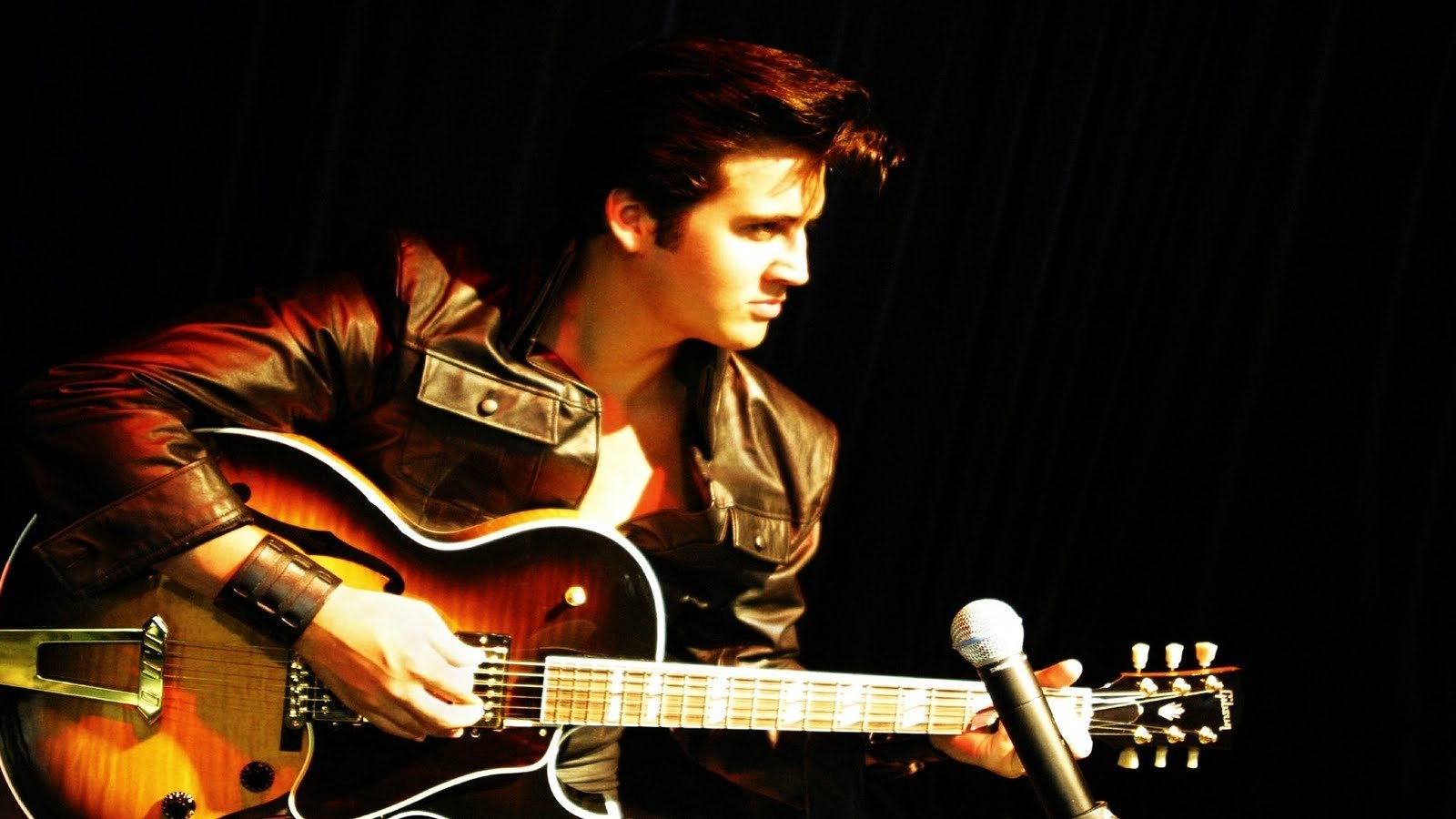 A musician styled as Elvis Presley plays an electric guitar, dressed in a leather jacket, exuding charisma and focus against a dark backdrop.