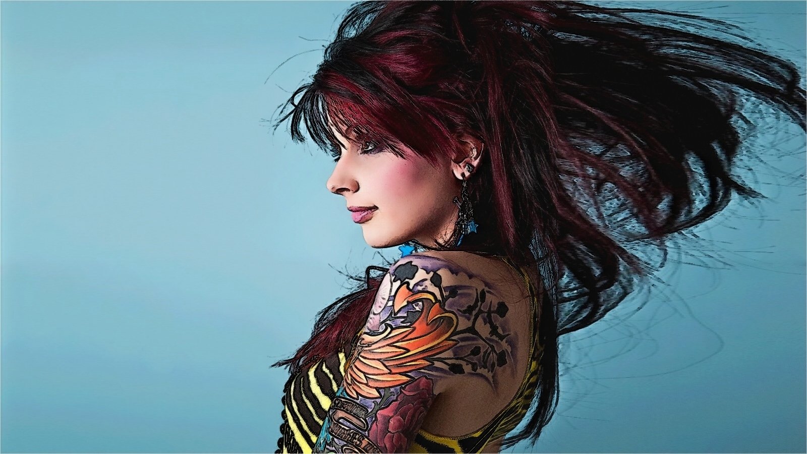 A woman with dark hair in motion showcases a colorful tattoo sleeve on her arm against a blue background.