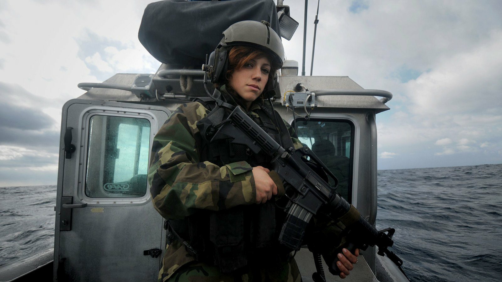 A woman in military gear stands on a boat at sea, confidently holding a gun, showcasing strength in the military context.