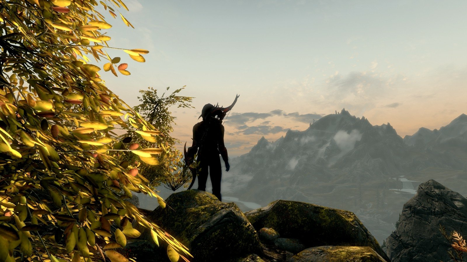 A character wearing a horned helmet stands on a rocky cliff overlooking a mountainous landscape in The Elder Scrolls V: Skyrim.