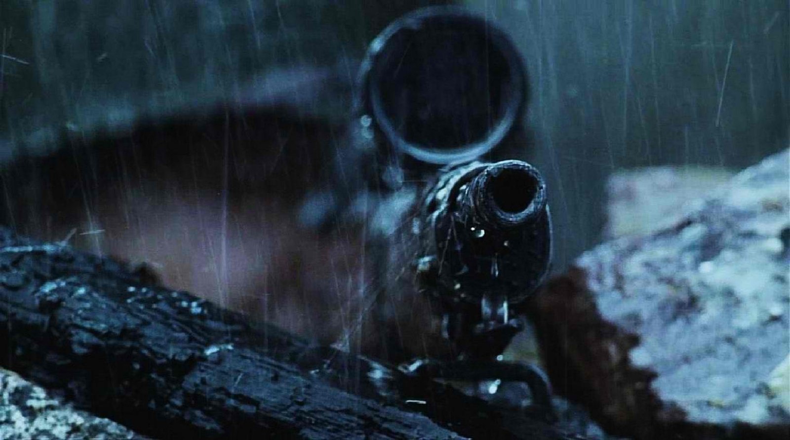 A close-up view of a sniper rifle resting on a charred log, with rain falling in the background, captures the fusion of man-made technology and nature's elements.