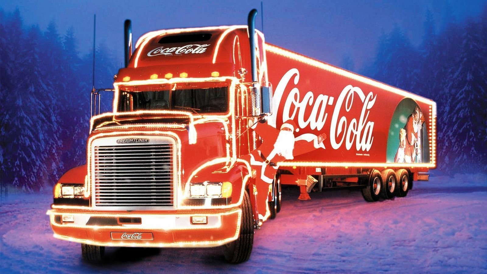 A man-made Coca-Cola holiday truck illuminated with bright lights, set against a snowy, nighttime forest background.