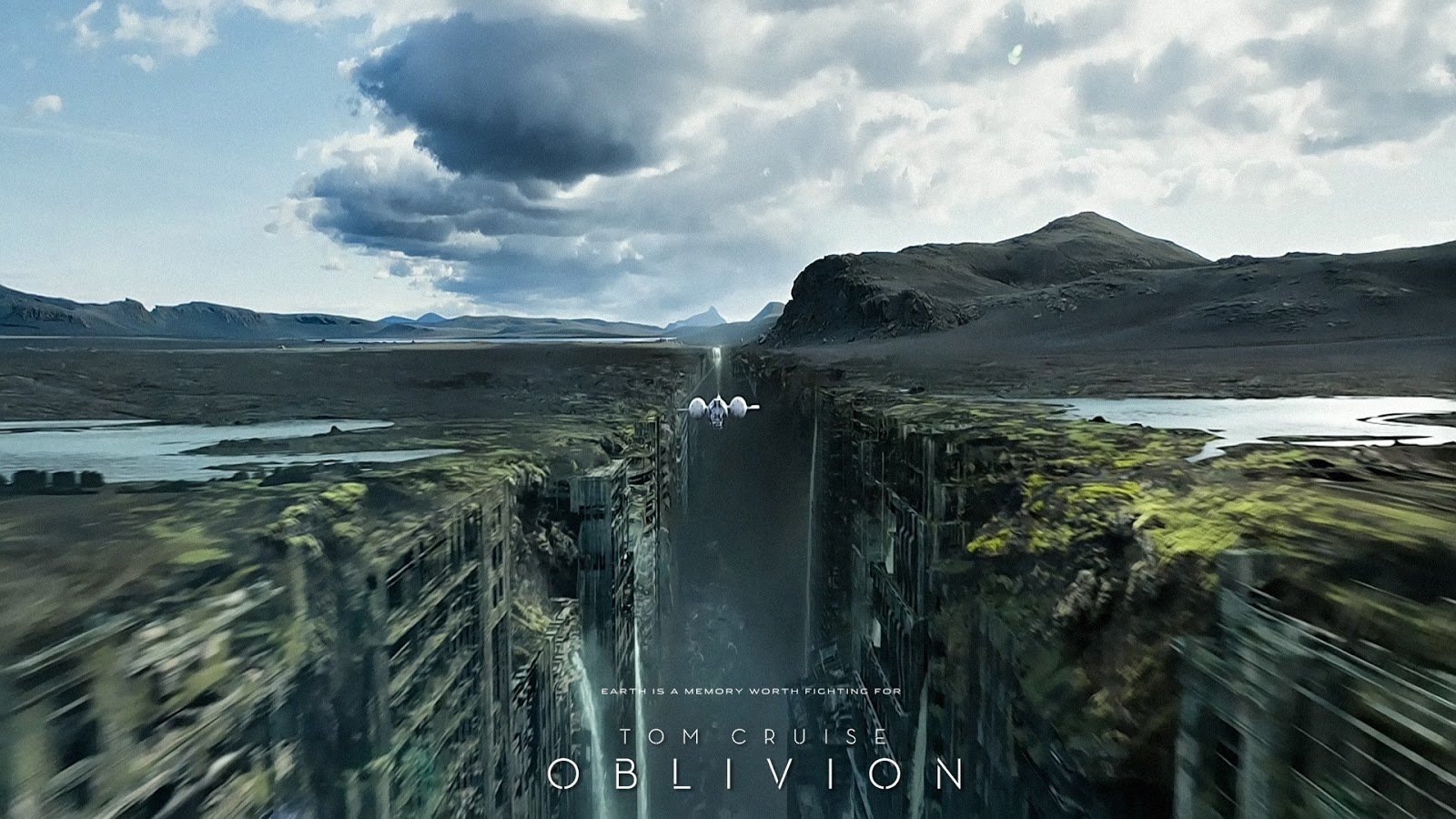 Oblivion (2013) movie scene: a vast fractured canyon splits a barren plateau, a tall waterfall plunging between cliffs beneath a dramatic cloudy sky.