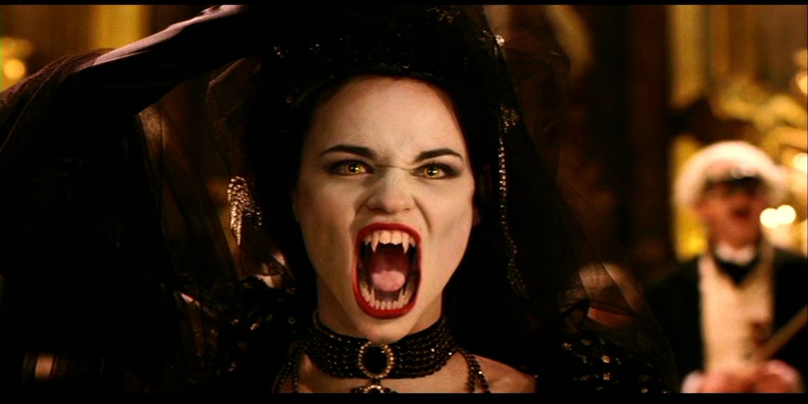 A fierce vampire with fangs bared and a striking black costume screams in a dramatic scene from the movie Van Helsing. The atmosphere is both haunting and powerful.