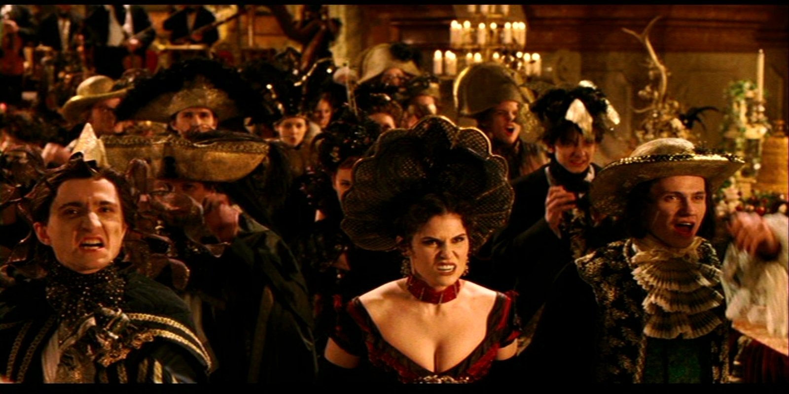 A dramatic scene from the movie Van Helsing, featuring a crowd dressed in elaborate costumes, with characters displaying various intense expressions amidst a lavish setting.