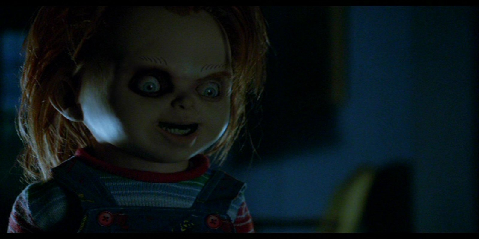 Chucky, the sinister doll from the movie Curse of Chucky, grins menacingly in a dark, eerie setting.