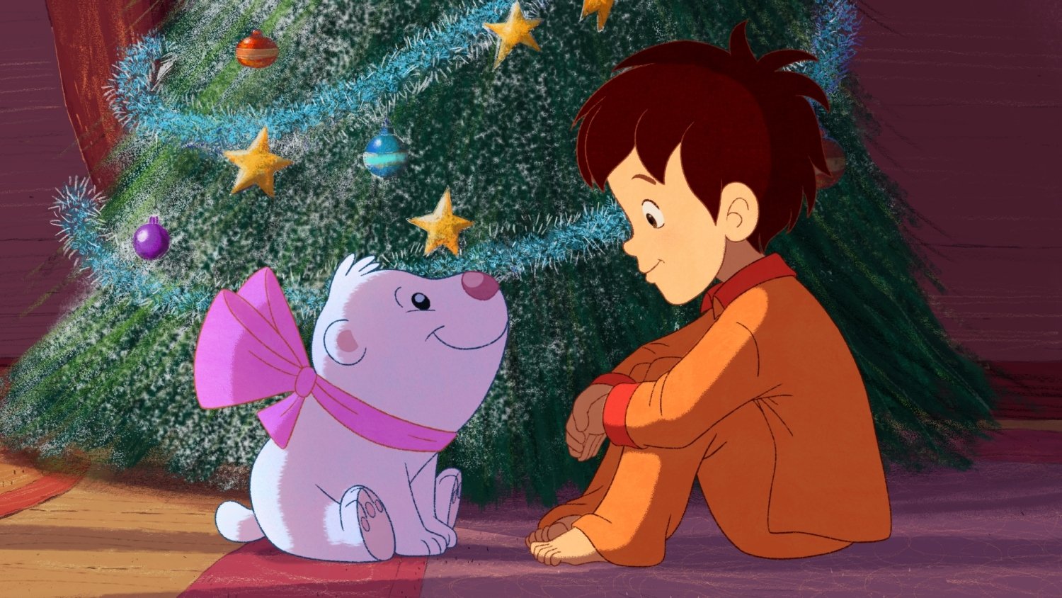 Scene from the movie Santa's Apprentice showing a young boy in orange pajamas sitting on the floor, facing a small white dog with a large pink bow near a decorated Christmas tree.