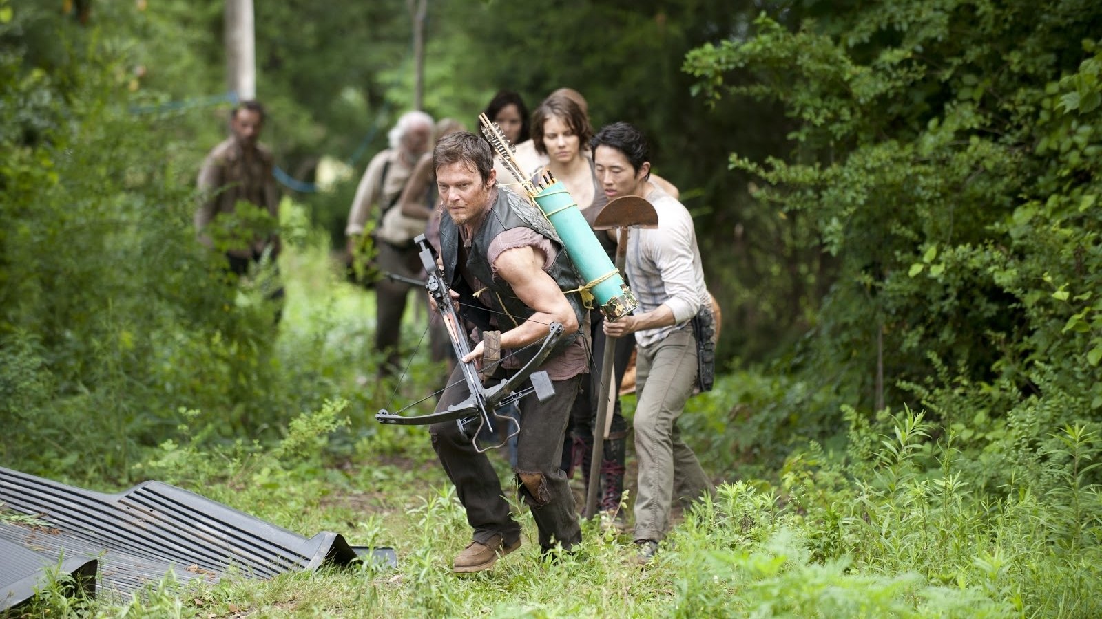 Norman Reedus as Daryl Dixon leads a group through a wooded area in a scene from the TV show The Walking Dead, highlighting their struggle for survival amid the undead.
