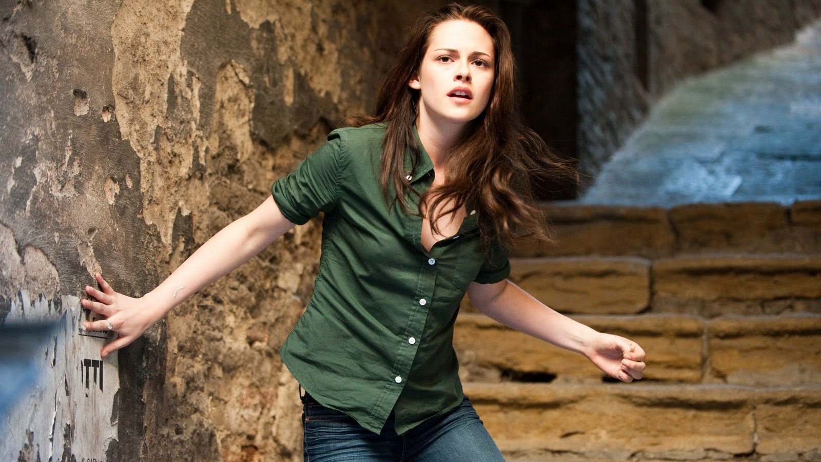 Kristen Stewart portrays Bella Swan in a tense moment from *The Twilight Saga: New Moon*, captured in an atmospheric stairwell setting.