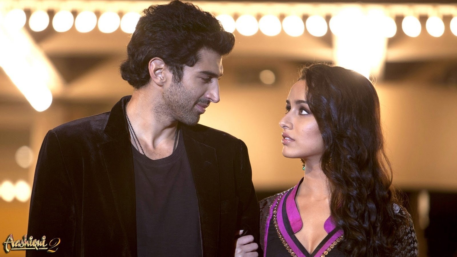 A romantic moment from the movie Aashiqui 2, featuring a man and woman gazing into each other's eyes, surrounded by soft lights that enhance the emotional atmosphere.