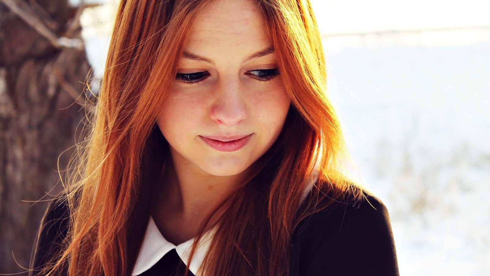 A woman with long, flowing hair and a subtle tattoo gazes thoughtfully downward, set against a serene winter backdrop.