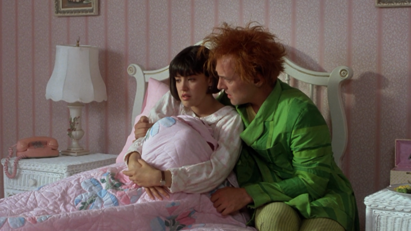 Phoebe Cates and Rik Mayall in a scene from the movie Drop Dead Fred, with Cates sitting on a bed and Mayall leaning close beside her.