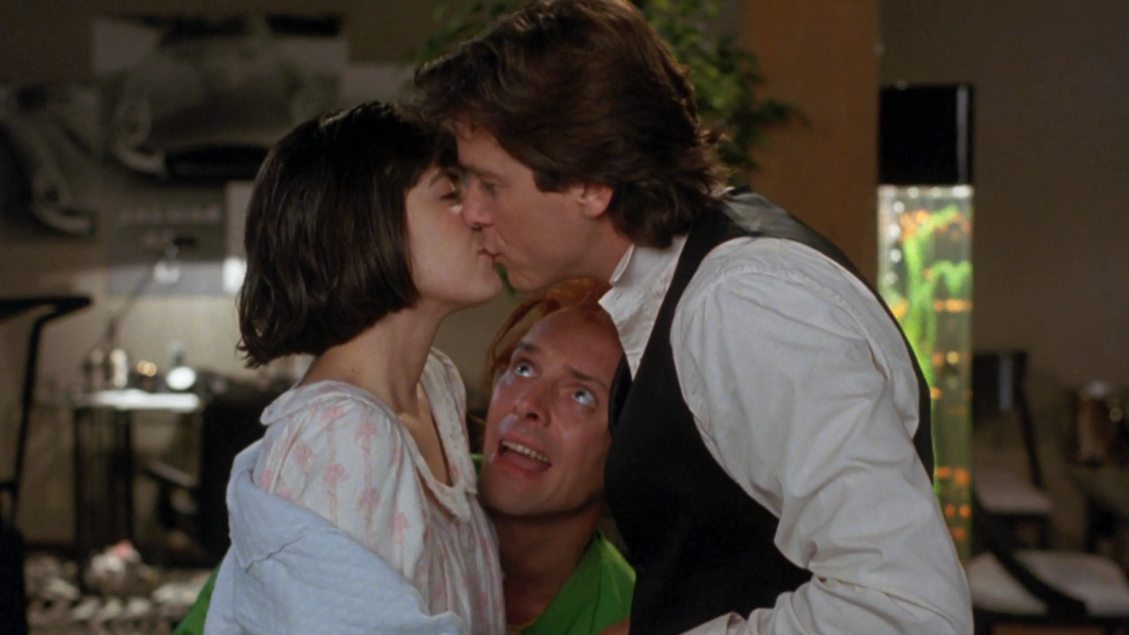 Phoebe Cates and Rik Mayall share a kiss in a scene from the movie Drop Dead Fred, with a third character looking up at them.