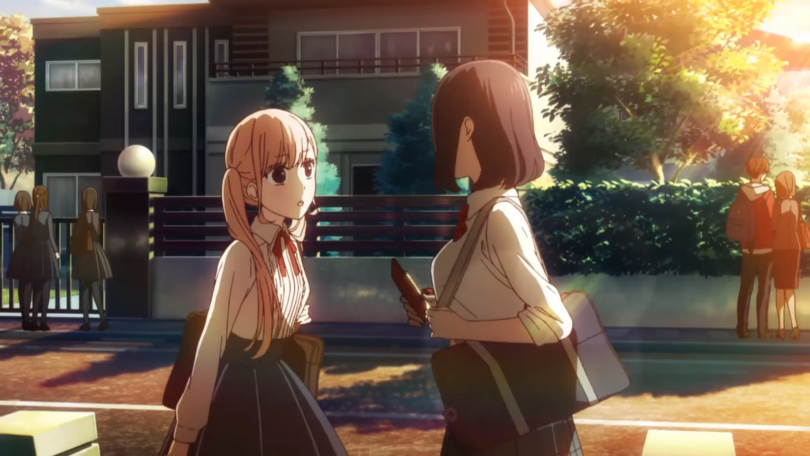 Lilina Sanada and Misaki Takasaki from the anime Love and Lies stand facing each other on a sunlit street with a school and trees in the background.