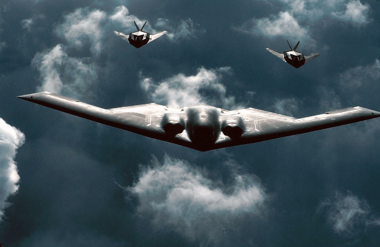 Two Northrop Grumman B-2 Spirit stealth aircraft fly through a cloudy sky, showcasing their unique design and military capabilities.