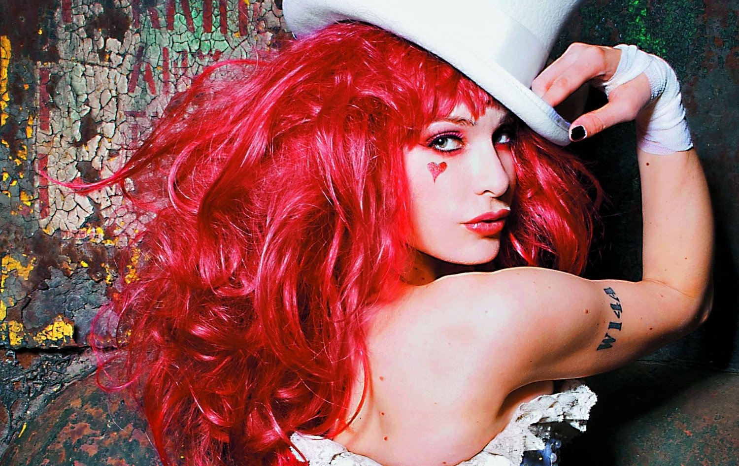 Emilie Autumn with vibrant red hair poses confidently, wearing a white top hat and corset, embodying her unique musical and theatrical style.