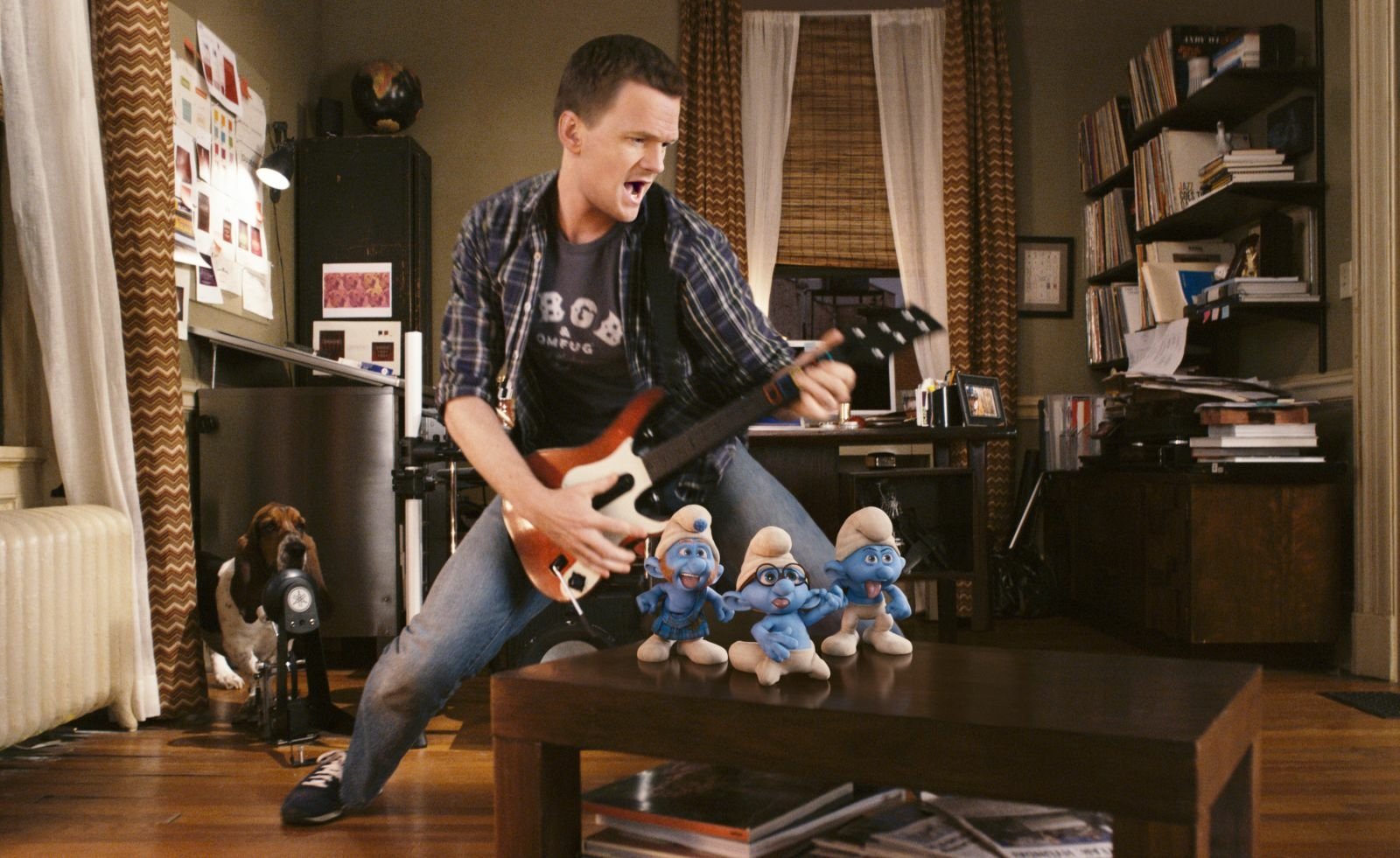 Man air-guitars in a living room as three Smurfs from the movie The Smurfs sit on a coffee table.