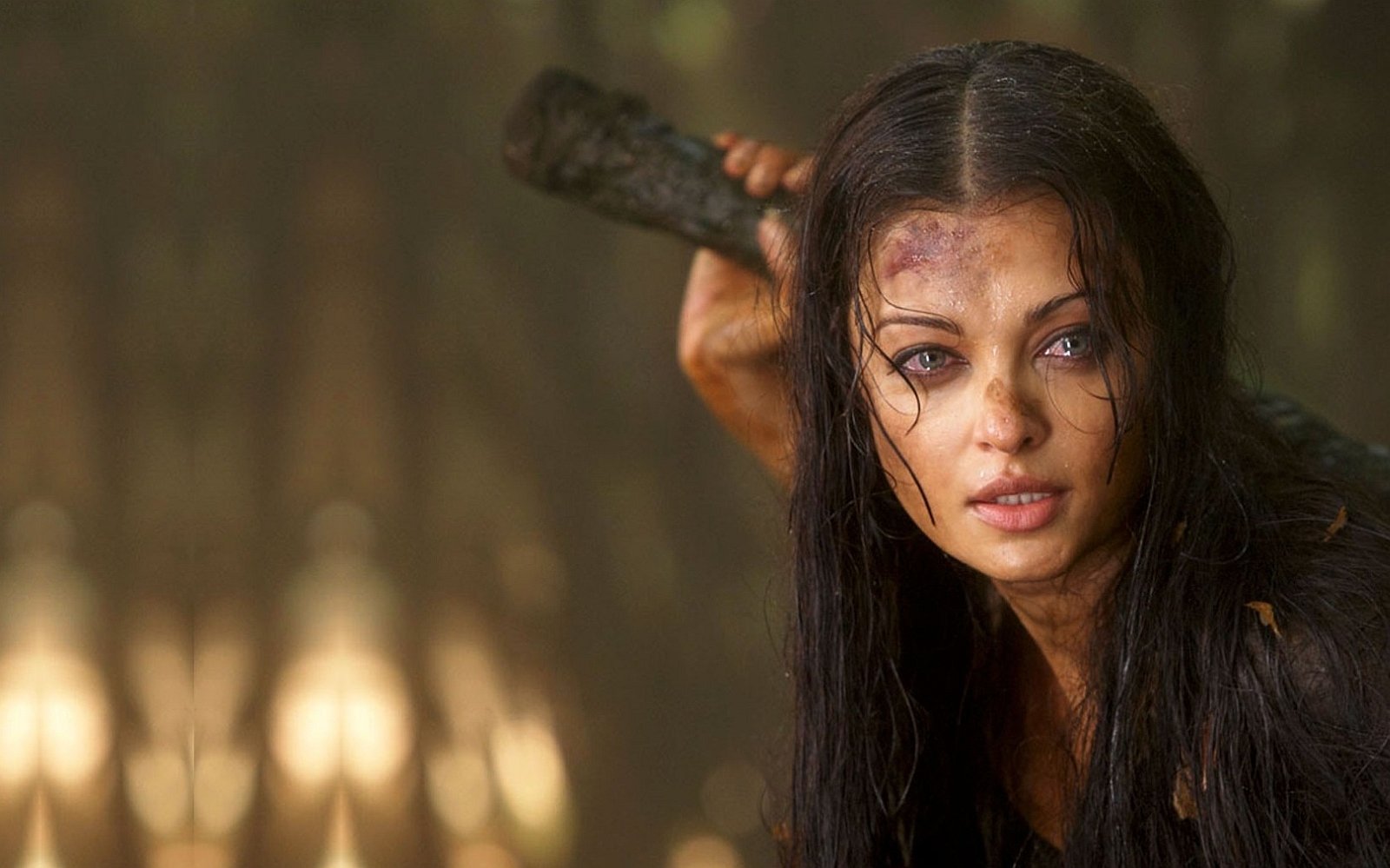 Aishwarya Rai, a renowned celebrity, appears with wet hair and a determined expression, gripping a stick amidst a natural, dimly lit setting.