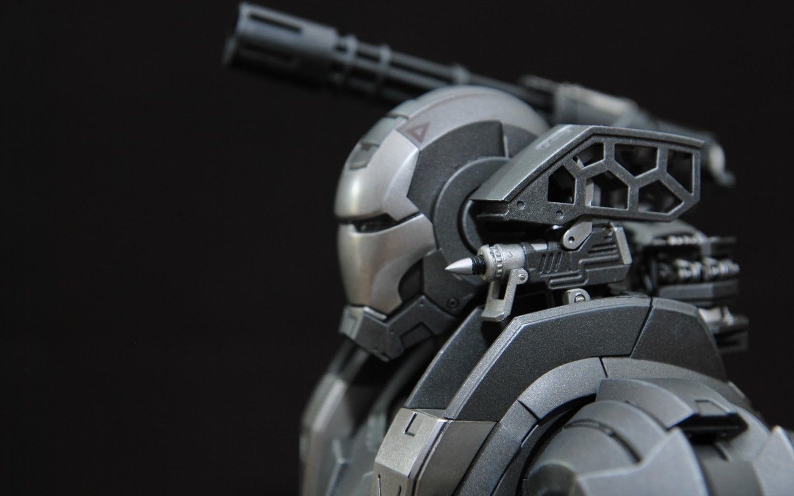 Close-up of War Machine armor from the Iron Man comic, featuring a detailed helmet and mounted shoulder cannon against a dark background.