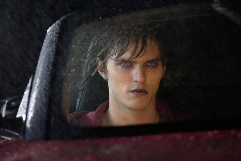 Nicholas Hoult stares intently from a car's side mirror, his striking blue eyes contrasting with a rainy backdrop, capturing a moment from the movie Warm Bodies.