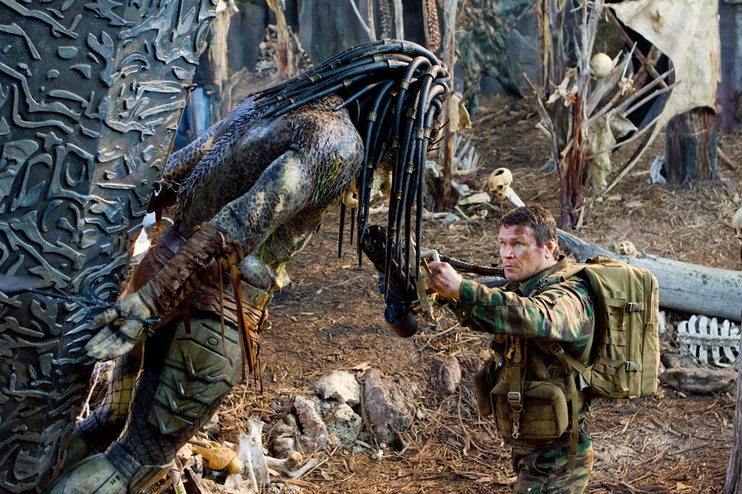 A soldier aiming a gun at an armored alien creature in a dense forest, a tense moment from the movie Predators.