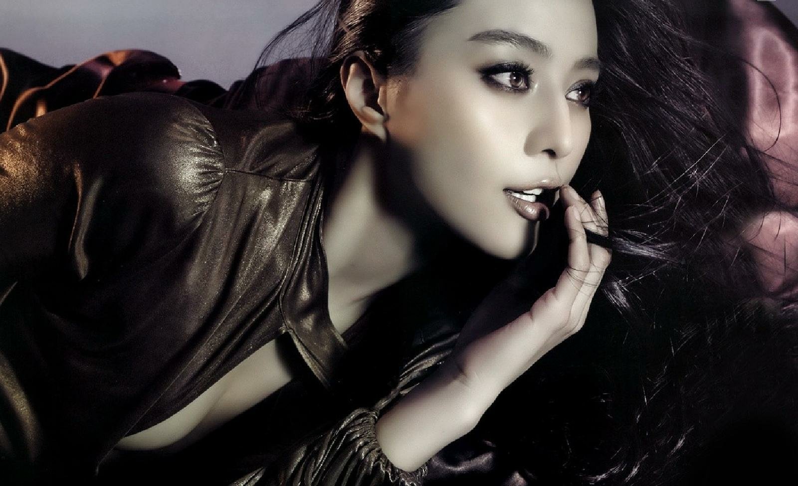 Portrait of celebrity Fan Bingbing with flowing hair, wearing a dark outfit, captured in a dramatic, moody lighting.