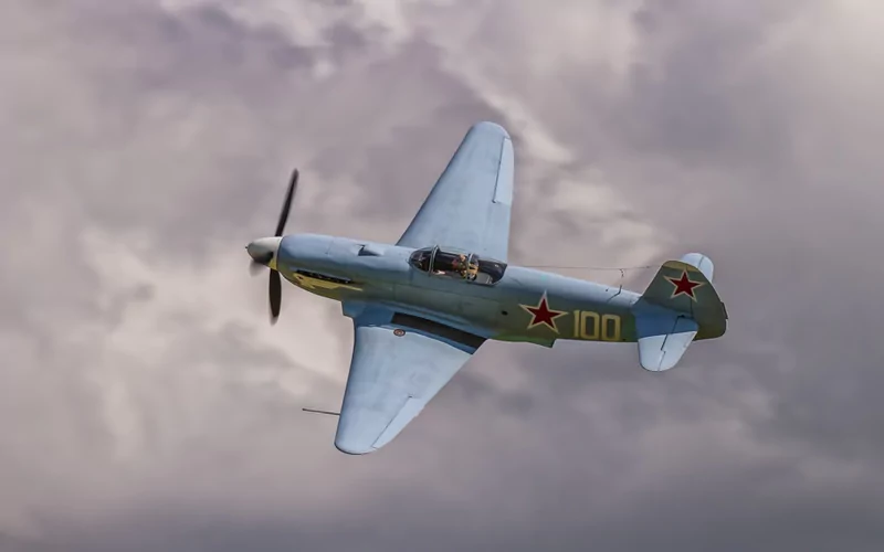 A military aircraft with Soviet star insignia flies against a cloudy sky.