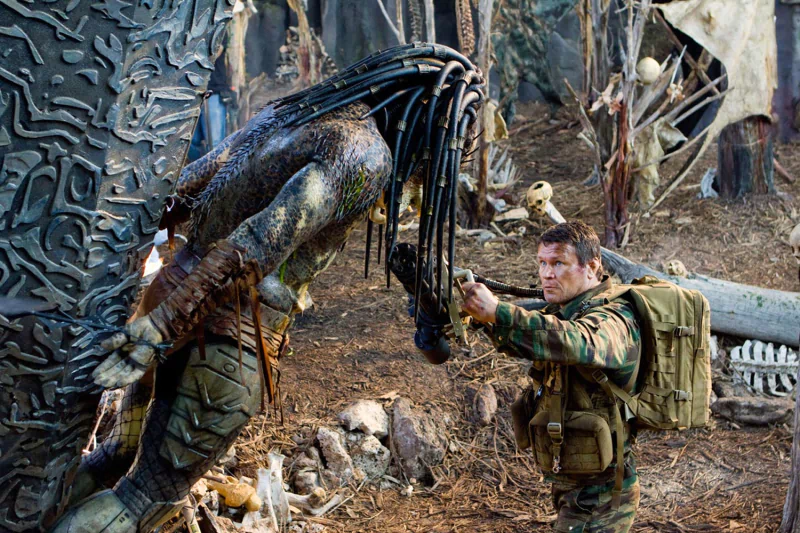 A soldier aiming a gun at an armored alien creature in a dense forest, a tense moment from the movie Predators.