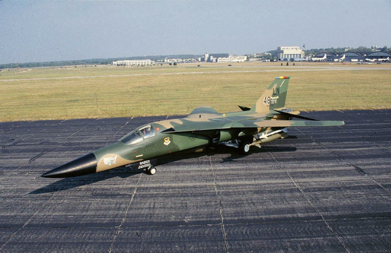 Military jet General Dynamics F-111 Aardvark parked on a runway with open exhaust nozzles and a blurred airfield background.