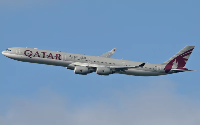 A Qatar Airways Airbus A340 aircraft in flight against a clear blue sky.