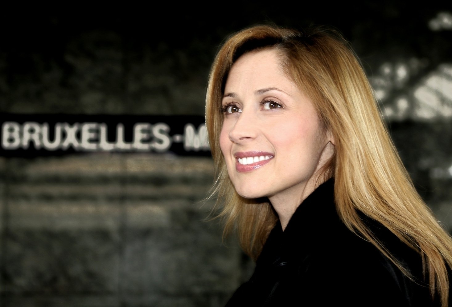 Portrait of Lara Fabian smiling, with a blurred background featuring the text BRUXELLES-M. The image is associated with music and the artist Lara Fabian.