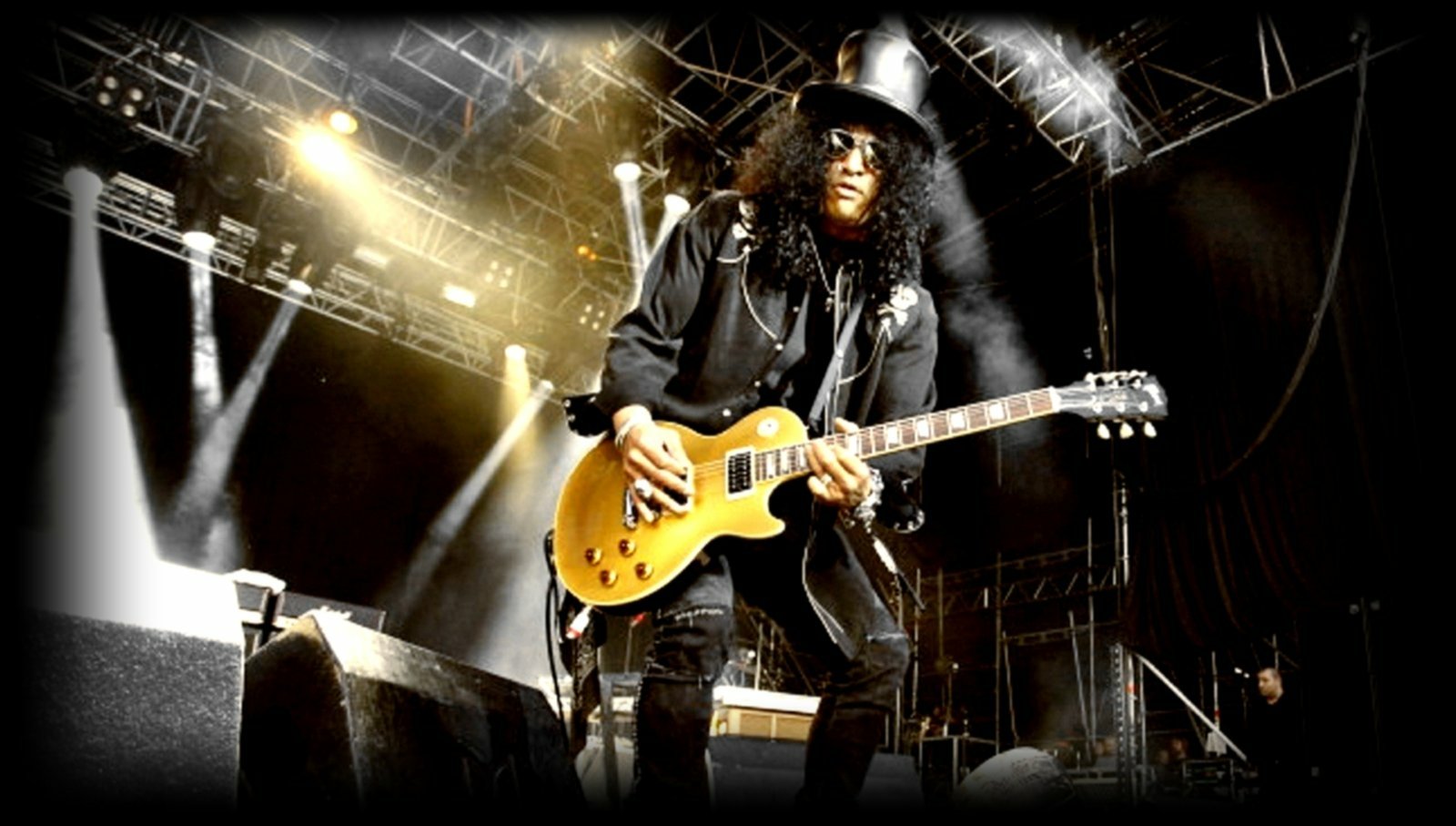 Slash performs on stage with a spotlight highlighting his iconic top hat and guitar during a live music concert.