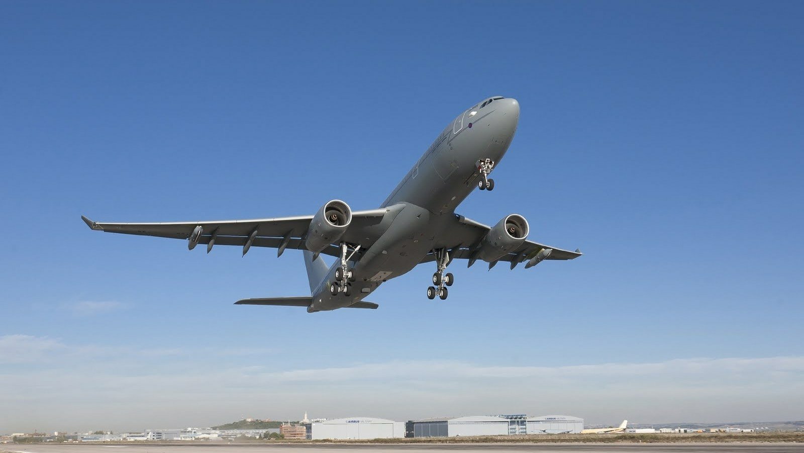 An Airbus A330 aircraft ascending against a clear blue sky above an airport runway.