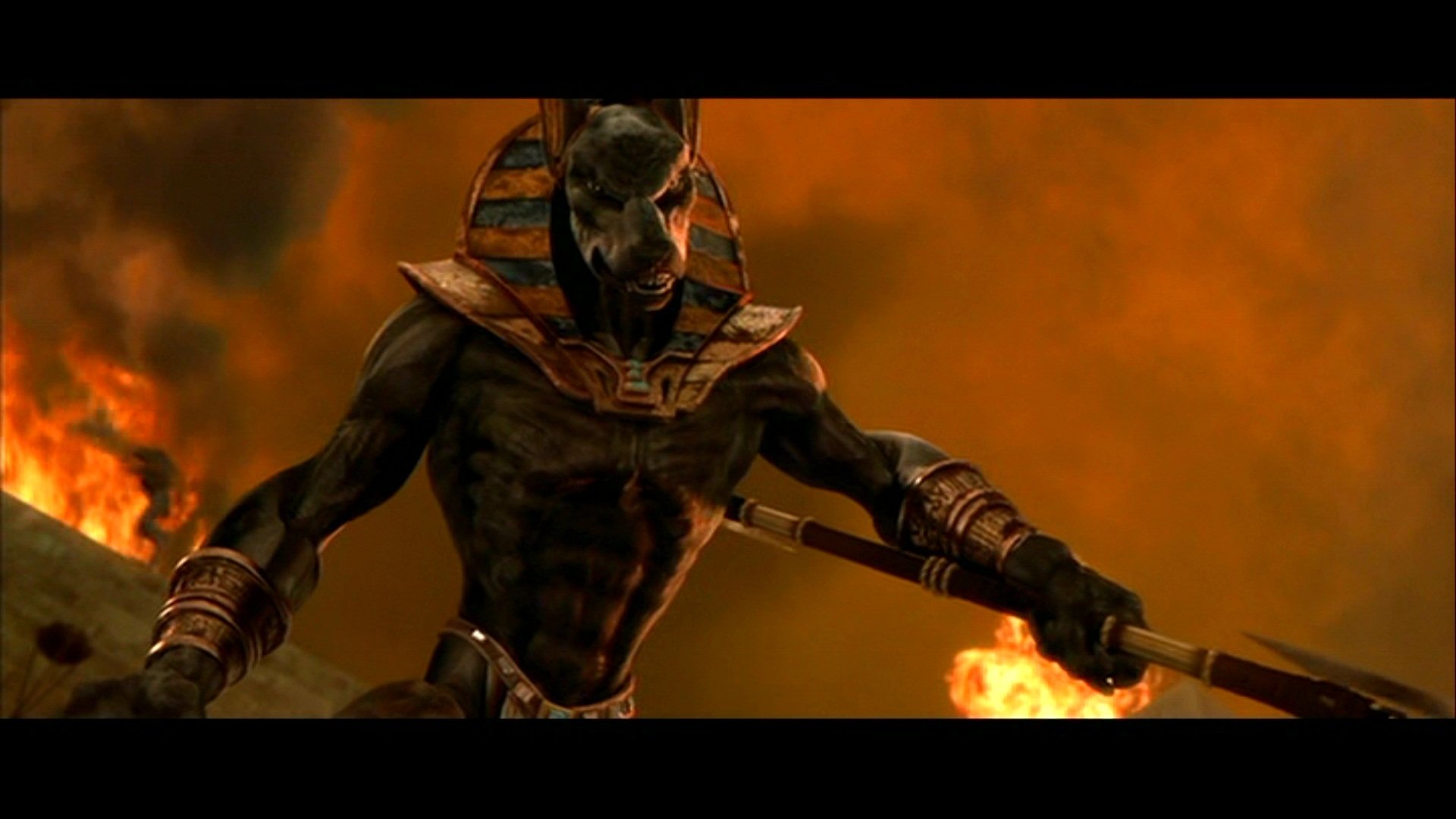 Armored, jackal-masked pharaoh-like warrior grips a spear amid roaring flames — a dramatic scene from the movie The Mummy Returns.