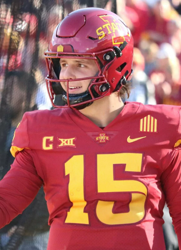 Football player in maroon jersey number 15 standing on the field during a sunny sports event.