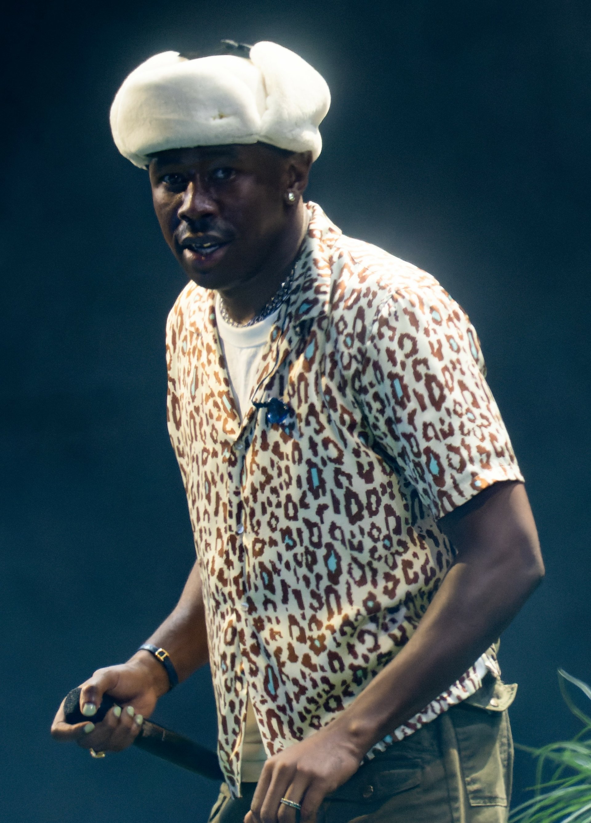 Rapper on stage with a leopard print shirt and a unique white hat during a music performance
