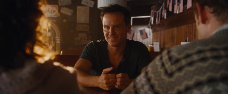 A tense scene from the movie 'All of Us Are Strangers' with a man in a green shirt sitting at a bar, facing two individuals and engaging in a serious conversation.