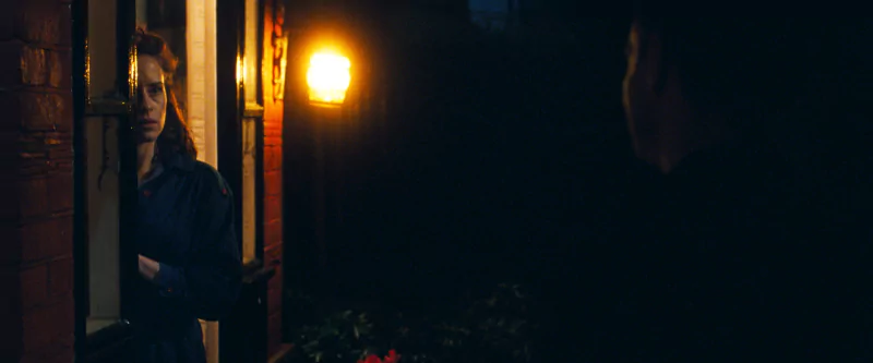 Tense scene from All of Us Are Strangers movie showing a woman looking warily at a shadowy figure outside.