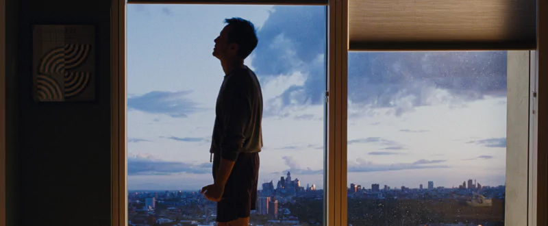 Man silhouetted against window overlooking cityscape in a scene from All of Us Are Strangers movie.