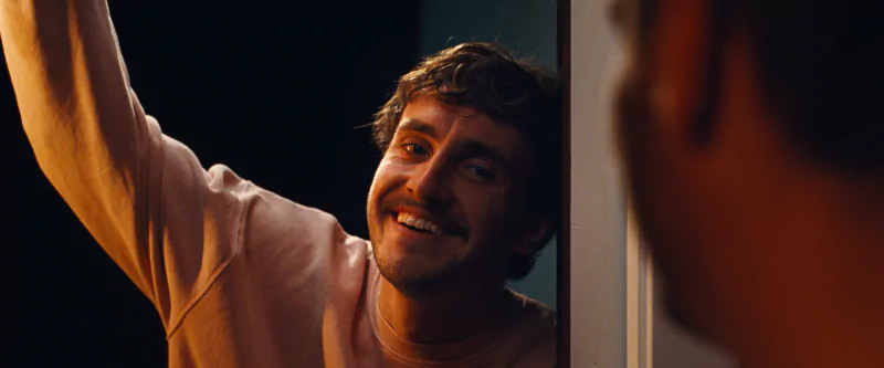 A smiling man interacting with another person off-camera in a scene from the movie All of Us Are Strangers.