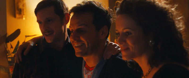 Scene from the movie All of Us Strangers showing three actors sharing a warm moment in a dimly lit room, conveying the emotional depth of the film.