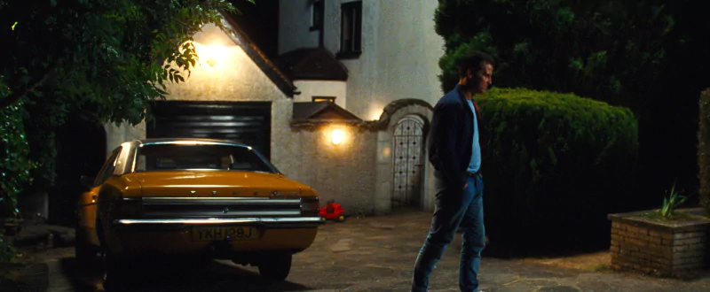 Scene from All of Us Are Strangers movie showing a character walking past a vintage car parked outside a house at night.