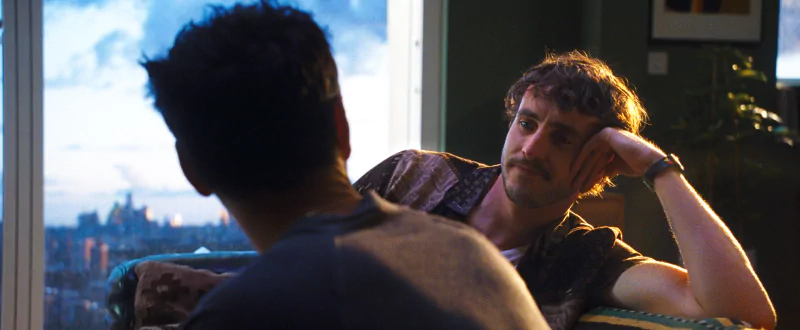 Two characters having a conversation in a scene from the movie All of Us Strangers with a city skyline in the background at dusk.
