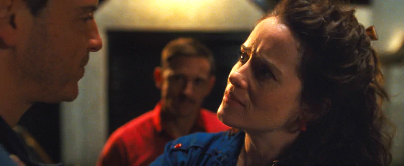 Intense scene from the movie All of Us Are Strangers showing a close-up of a man and woman in a serious conversation with another person in the background.